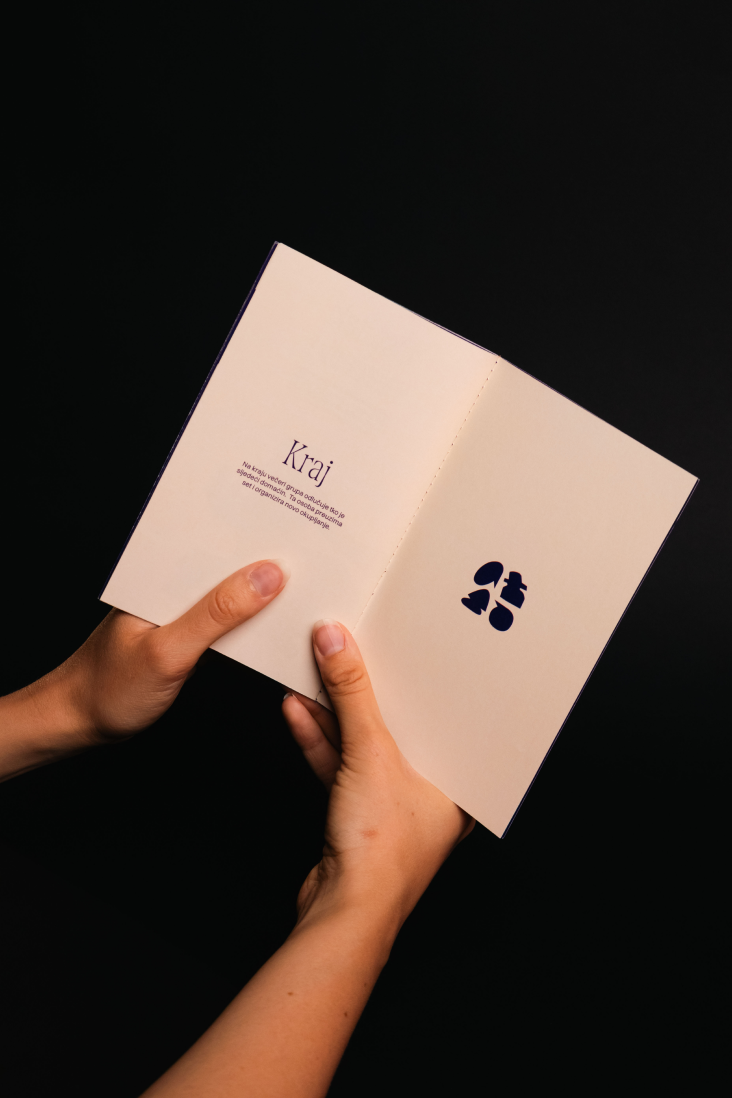 Hands holding the cream project booklet against a black background