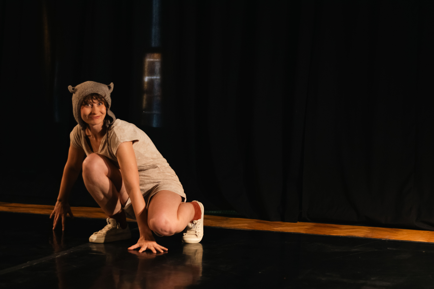 Costumed performer crouching on a dark theatre stage