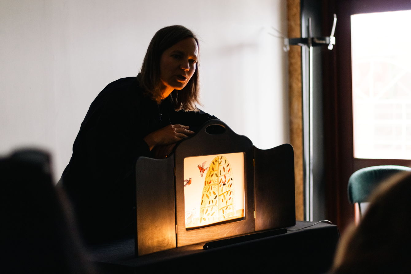 Performer presenting an illuminated shadow theatre scene