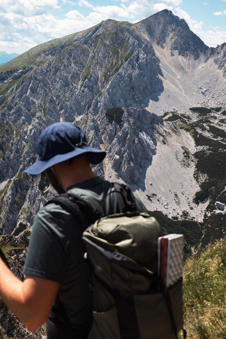 Hiker looking down while standing before a mountain ridge