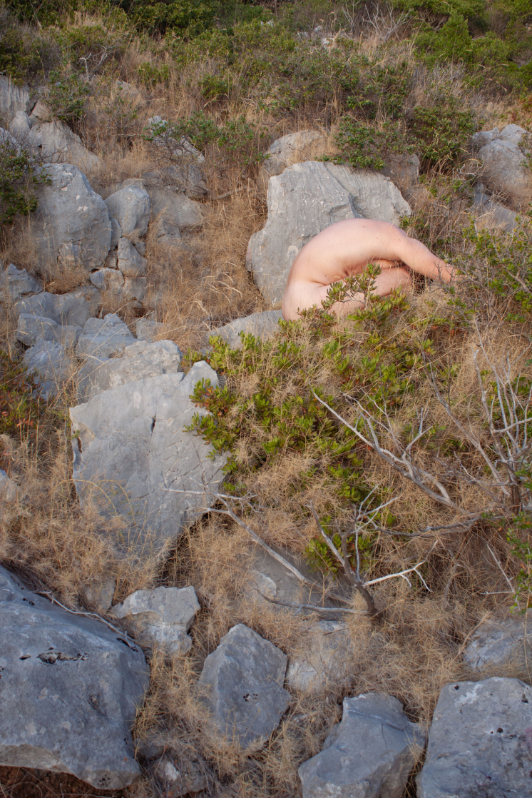 Human figure merging visually with rocks and Mediterranean vegetation