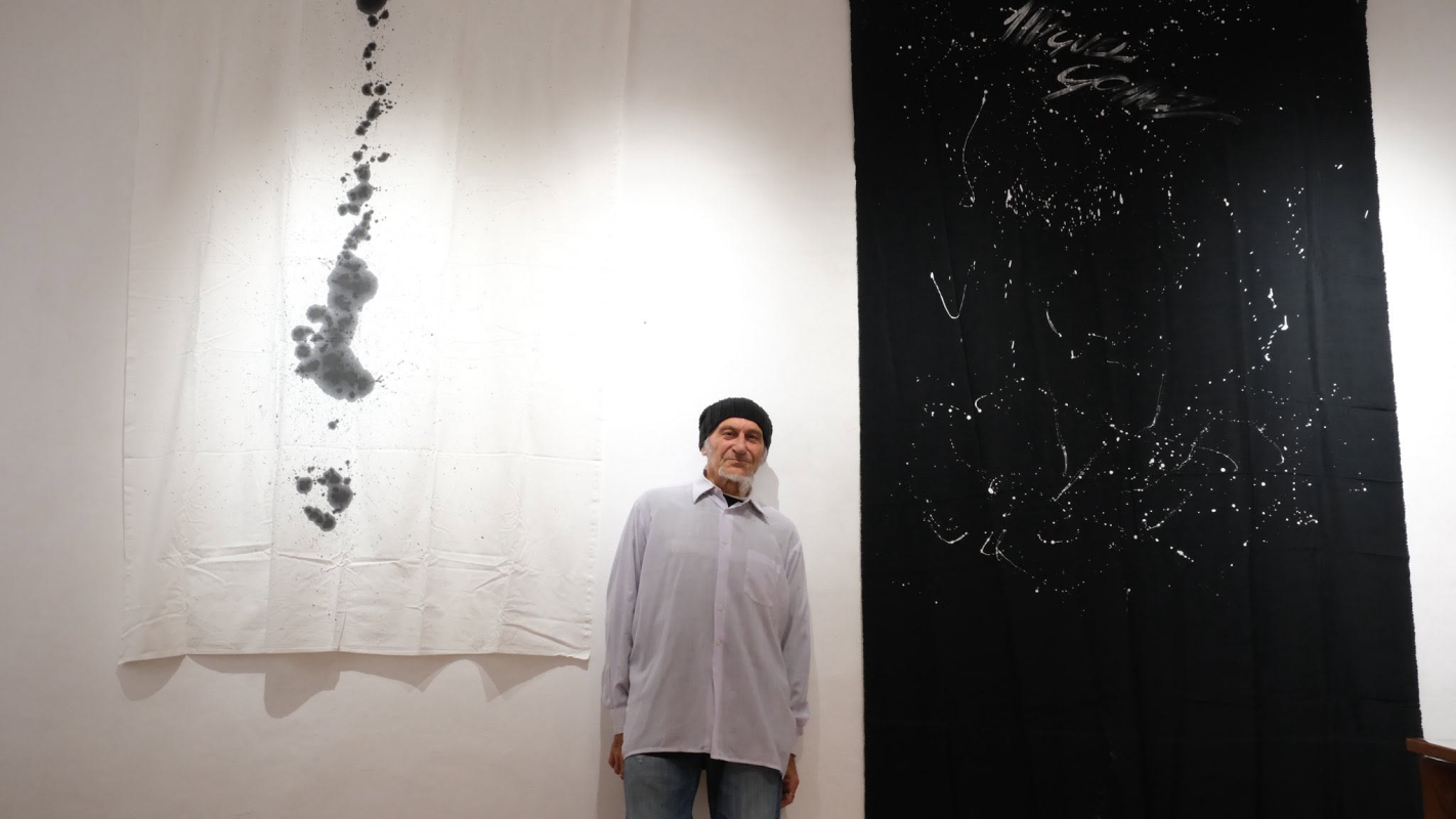 Artist standing between black and white works during the SUFFEST exhibition